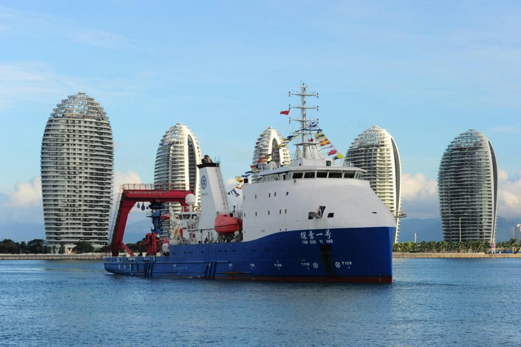 A modern cruise ship docked in the picturesque Sanya Bay, with iconic skyscrapers in the background.