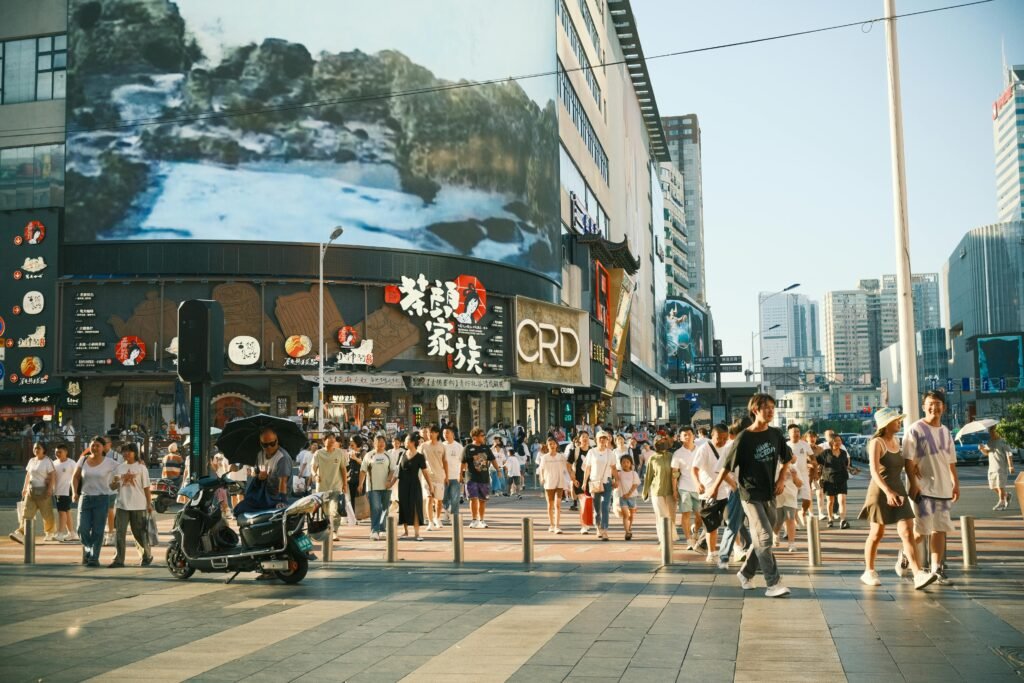 A vibrant urban street filled with people and colorful billboards on a sunny day.
