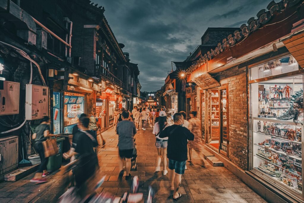 Vibrant nighttime street view of a busy alley in Beijing, China, with shops and people walking.