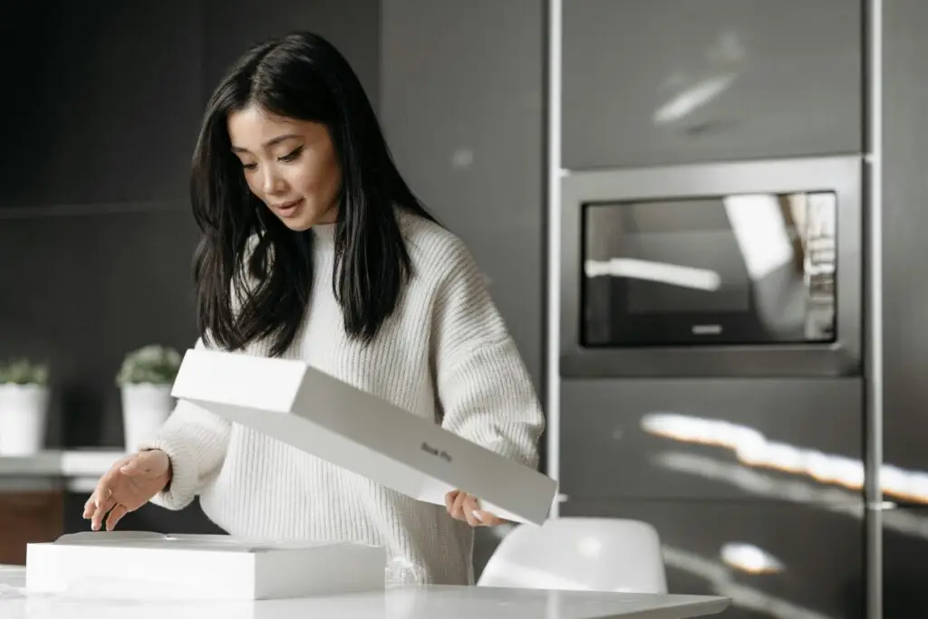 An asian woman excitedly unpacks a delivery box in her modern kitchen.